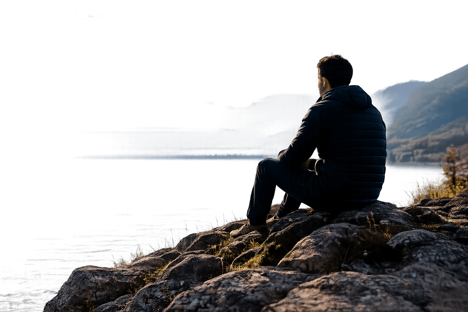 Person sitting beside a calm lake and mountains
